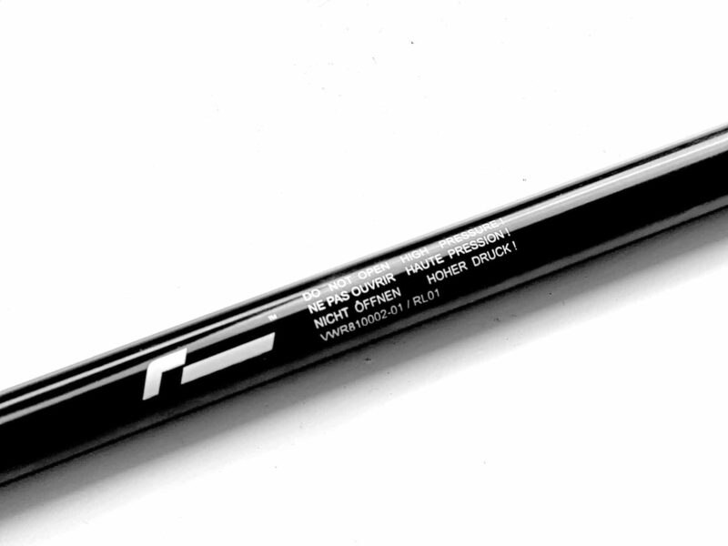 Close-up of a black cylindrical tube with a multilingual warning: 'Do not open – High pressure' along its length