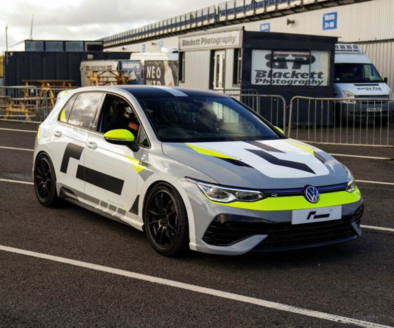 Racingline-Cup-Edition-EVO-Wheels-VWR610010_5-1jpg - OPSHOLDERS White race car with neon yellow accents parked on a race track, branding and photographers’ tent in background