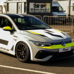 Racingline-Cup-Edition-EVO-Wheels-VWR610010_6-1jpg - OPSHOLDERS White Volkswagen race car with neon yellow accents and bold black graphics parked beside metal barriers at a race track area.