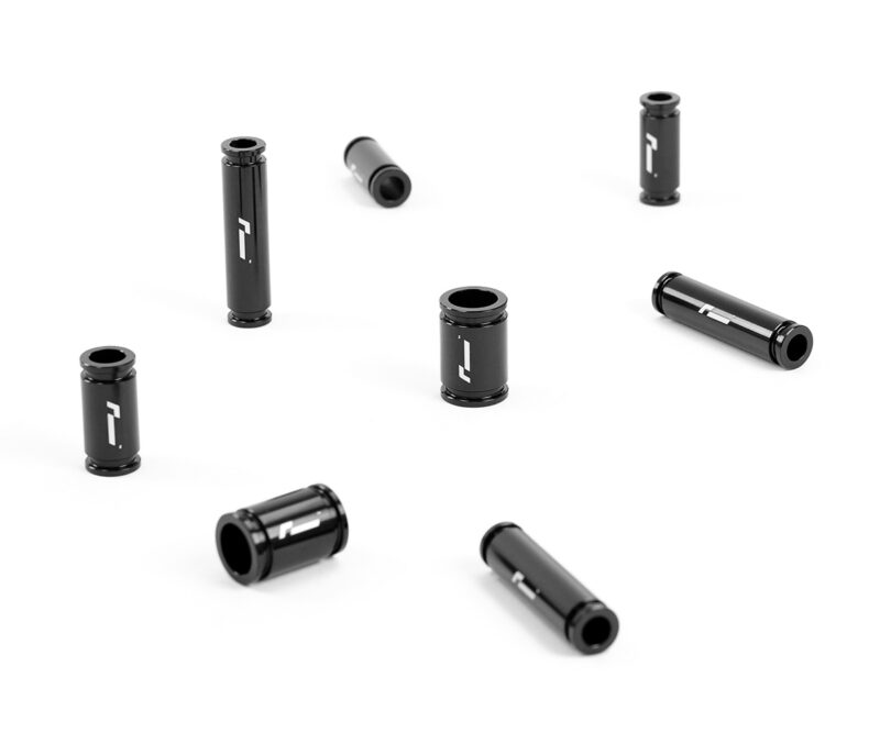 Racingline-DSG-Gearbox-Billet-Oil-Feed-Tubes-DQ500-DQ381-VWR040302_5jpg - OPSHOLDERS Several black cylindrical metal pieces with a white logo scattered on a white background, open ends visible for each tube, likely small adapters or spacers.