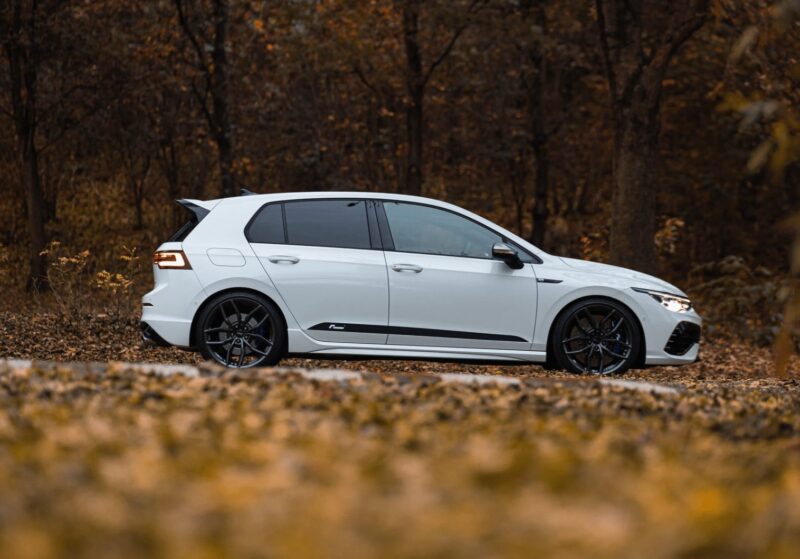 Racingline-Lowering-Springs-Mk8-R-1jpg - OPSHOLDERS White hatchback car parked on a leaf-covered road in a autumn forest, side view showing black wheels and dark-tinted windows.