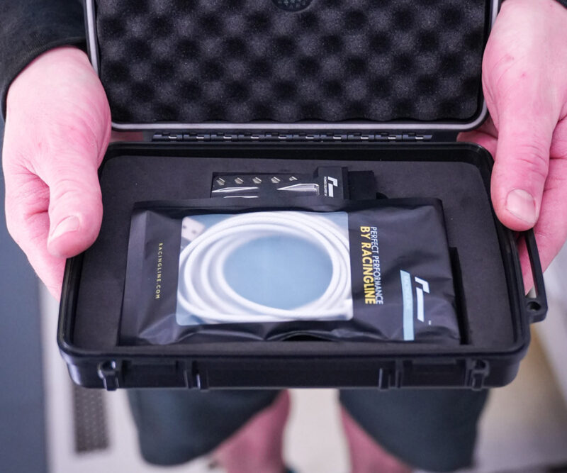 Racingline-PDM-Home-Tuning-VWR031000_6-1jpg - OPSHOLDERS Person holds an open protective case revealing a packaged racing accessory with a white circular coil and the 'RACINGLINE' branding visible inside.