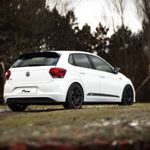 White VW hatchback viewed from rear three-quarter angle parked on a grassy roadside with a forest backdrop.