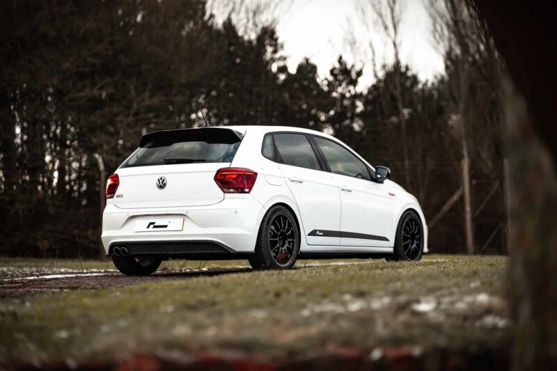 White VW hatchback viewed from rear three-quarter angle parked on a grassy roadside with a forest backdrop.