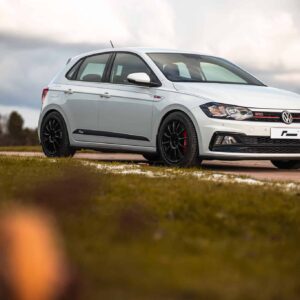White Volkswagen GTI hatchback parked on a rural road, with a cloudy sky in the background and grass nearby