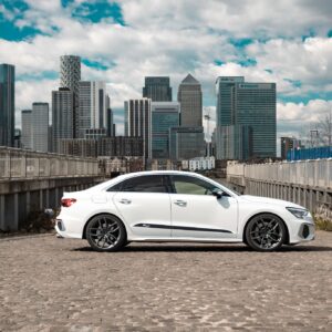 White sedan parked on a rooftop with a city skyline in the background under a blue sky with clouds