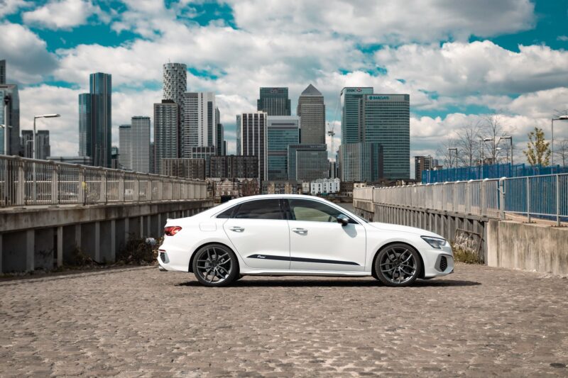 White sedan parked on a rooftop with a city skyline in the background under a blue sky with clouds