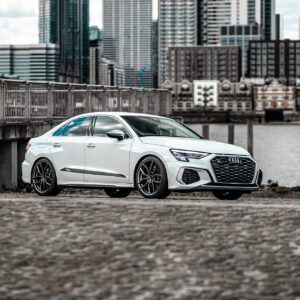 White Audi sedan parked on a waterfront with a city skyline in the background