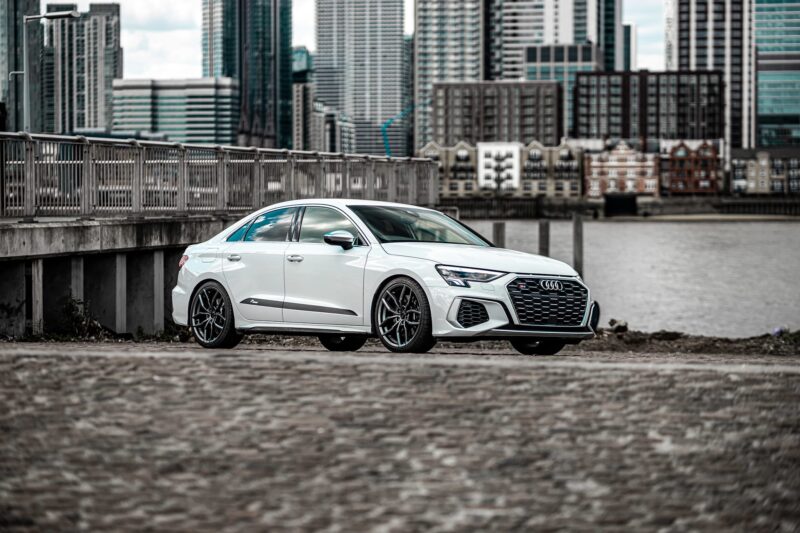 White Audi sedan parked on a waterfront with a city skyline in the background