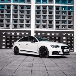 Racingline-S3-RS3-Lowering-Springs-1jpg - OPSHOLDERS White Audi RS sedan parked on a tiled plaza with a geometric, modern building behind it.