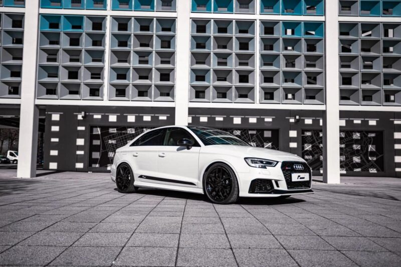 Racingline-S3-RS3-Lowering-Springs-1jpg - OPSHOLDERS White Audi RS sedan parked on a tiled plaza with a geometric, modern building behind it.