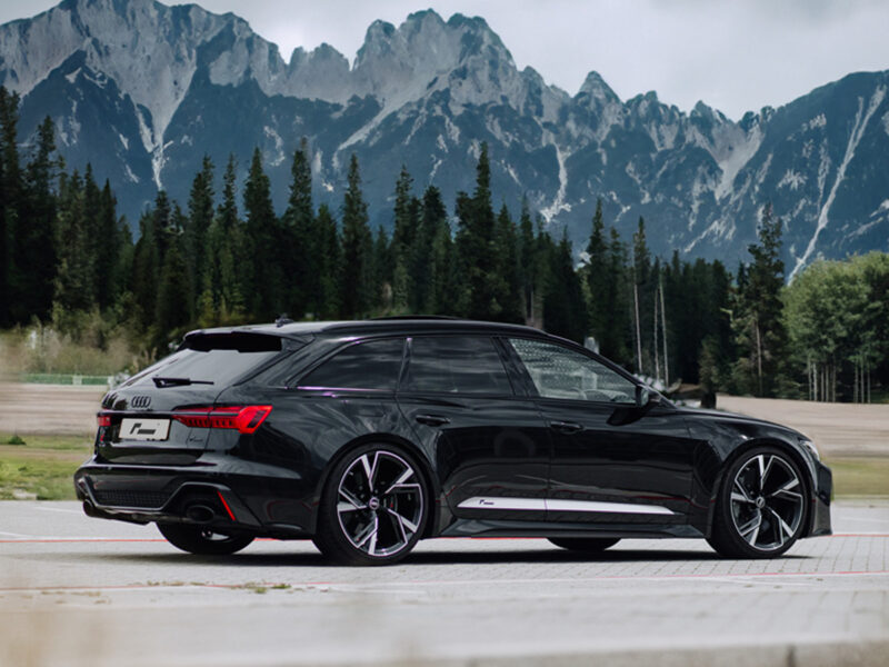 Racingline-VWR436001-fitted-1jpg - OPSHOLDERS Black luxury station wagon driving on a paved road with rugged mountains and pine trees in the background