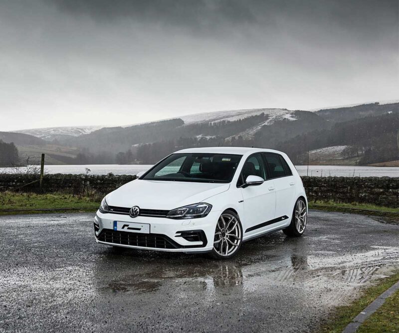 Racingline_Lowering_Springs_MK7R_2jpg - OPSHOLDERS White Volkswagen hatchback parked on a wet asphalt road with a misty, hilly landscape in the background under a cloudy sky.