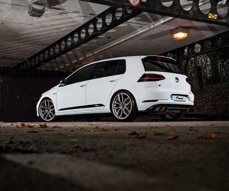 Racingline_Lowering_Springs_MK7R_3jpg - OPSHOLDERS White Volkswagen Golf R hatchback parked under an industrial overhead structure, viewed from the side/rear.