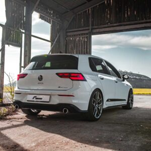 Racingline_MK8_GTIjpg - OPSHOLDERS Rear three-quarter view of a white Volkswagen Golf GTI wagon parked inside a dilapidated shed with rusted metal beams in the background.