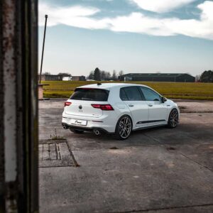 Racingline_MK8_GTI_1jpg - OPSHOLDERS Rear three-quarter view of a white VW Golf GTI Estate parked on a cracked concrete area with open fields and hangars in the distance.