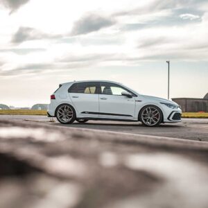 Racingline_MK8_GTI_2jpg - OPSHOLDERS White sporty hatchback parked on an airstrip, with hangars and an open sky in the background.
