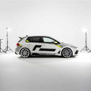 White hatchback car with black racing decals in a white photography studio surrounded by studio lights.