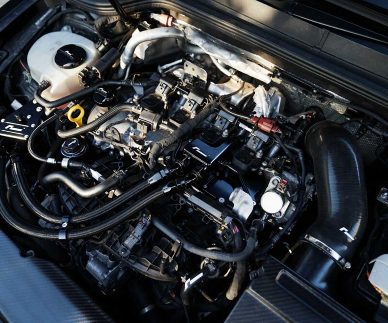 Close-up of a car engine bay showing hoses, cables, and fluid reservoirs with metal engine components visible