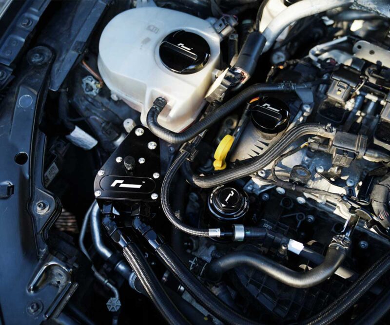 Close-up of a car engine bay with aftermarket black aluminum component and braided hoses.