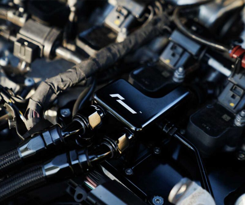 Close-up of a motorcycle's cockpit area showing a glossy black electronic unit with a white stylized logo.
