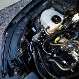 Close-up of a car engine bay showing an aftermarket aluminum strut brace and various hoses and fittings to the left and center of the image