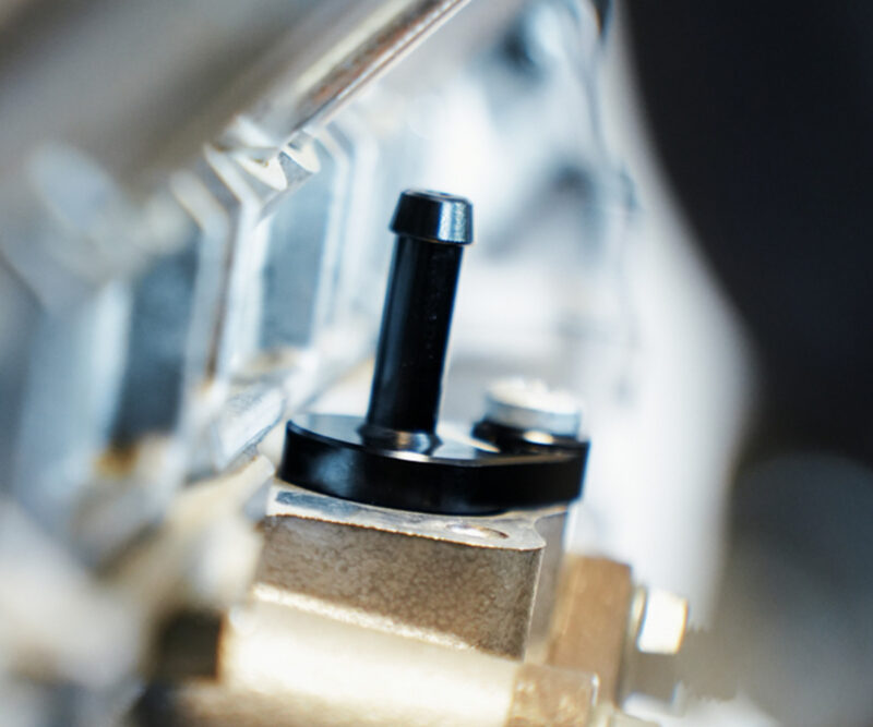 VWR140014_11-1jpg - OPSHOLDERS Close-up of a black vertical knob on an industrial machine with blurred metal surroundings
