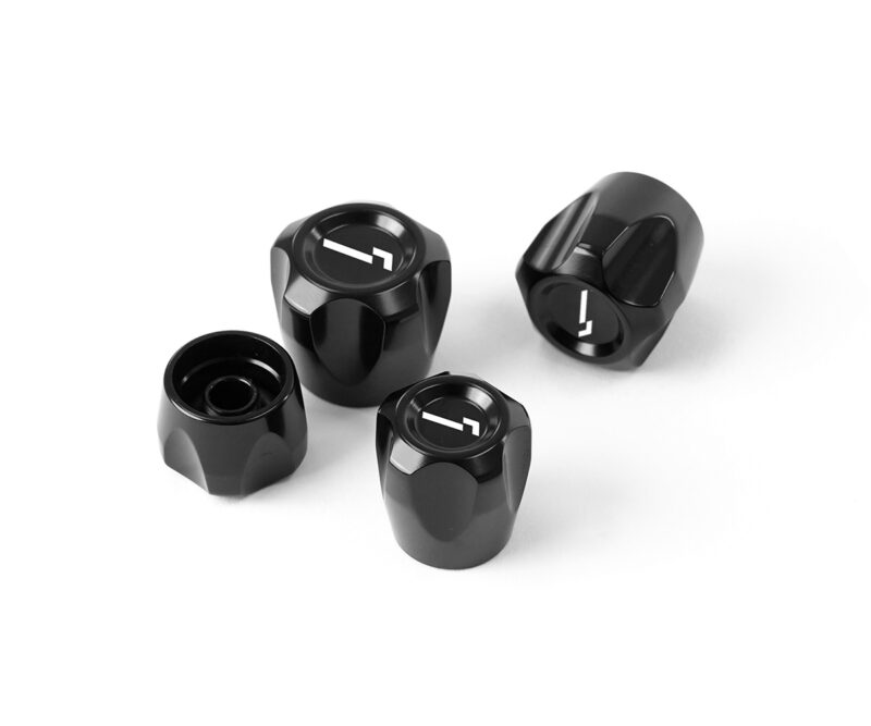 Four black glossy metal knobs with white indicators arranged on a white surface.