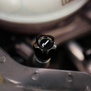 Close-up of a black, multi-lobed control knob with a white arrow mark in a car's engine bay