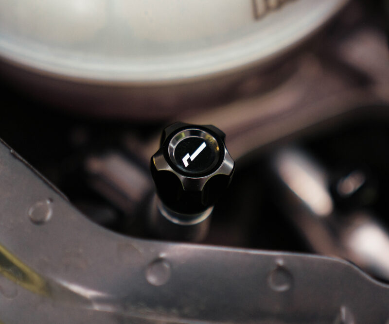 Close-up of a black, multi-lobed control knob with a white arrow mark in a car's engine bay