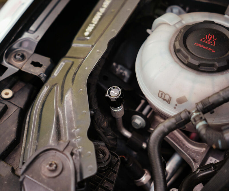Close-up of a car engine bay showing the coolant reservoir cap labeled 160 kPa/23 psi and surrounding hoses and components.