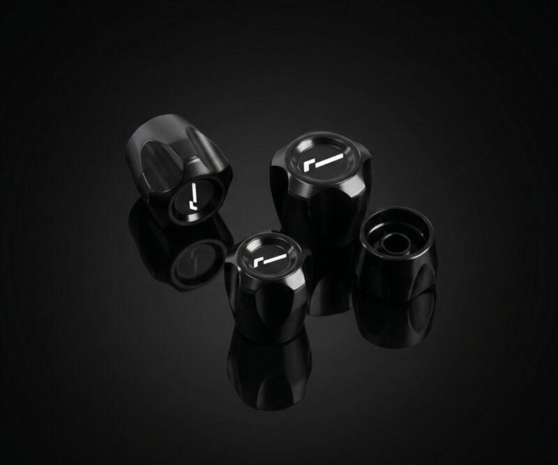 Set of four black glossy control knobs with white alignment marks arranged on a reflective black surface.