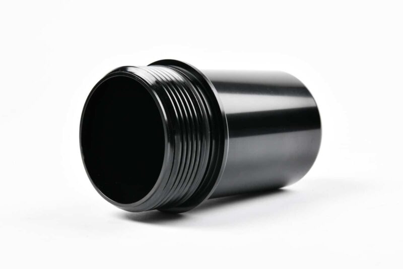 Black metal cylindrical tube with external threads on one end, resting on a white surface.