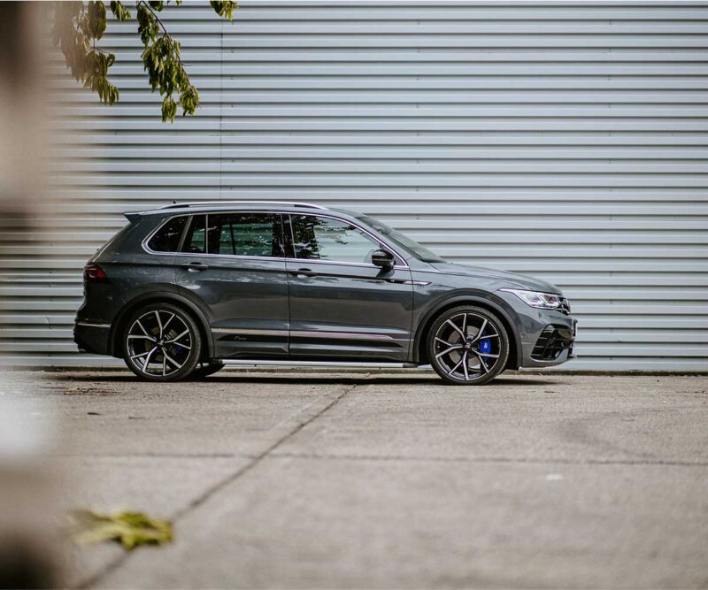 Side view of a dark-gray SUV parked on a concrete surface against a corrugated metal wall, chrome trim visible.