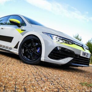 White sports car with neon yellow accents parked on gravel, low-angle shot showing black wheels and front grille