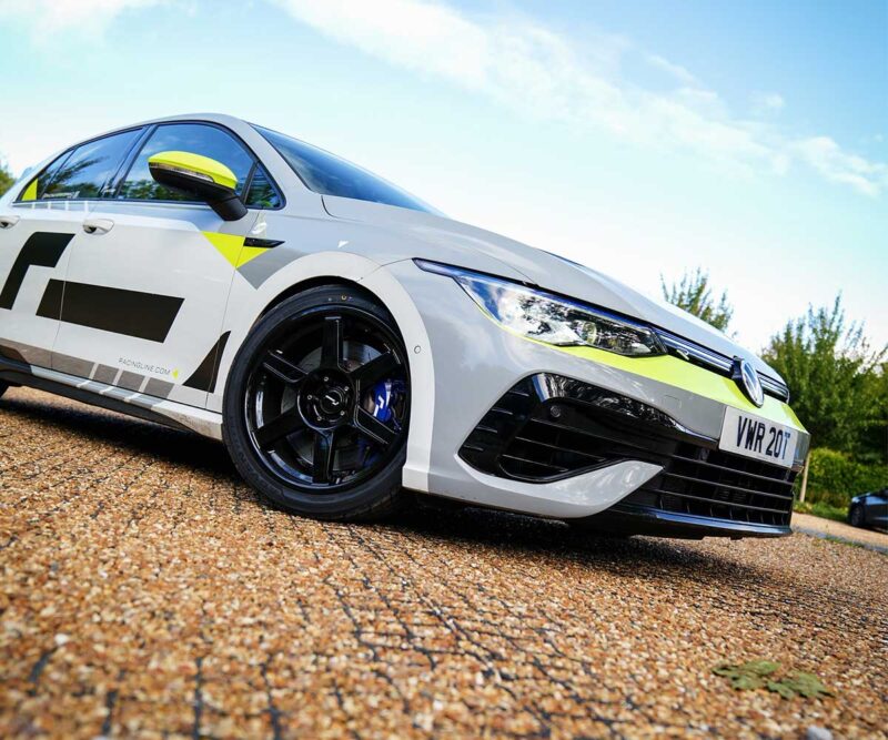 White sports car with neon yellow accents parked on gravel, low-angle shot showing black wheels and front grille