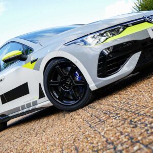 White sports/racing car with neon yellow accents on gravel, front grille and bold black wheels visible.