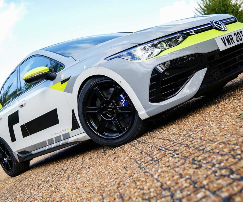 White sports/racing car with neon yellow accents on gravel, front grille and bold black wheels visible.
