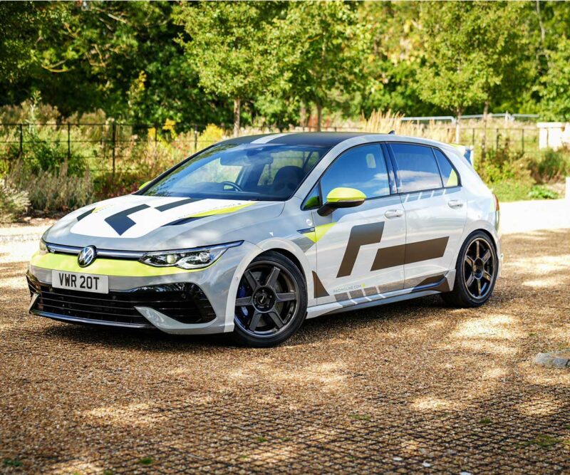 VWR610401_11jpg - OPSHOLDERS White Volkswagen hatchback with lime-green racing livery and bold geometric graphics, parked on gravel with trees in the background