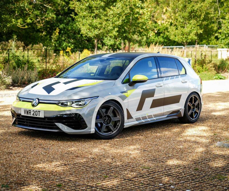VWR610401_12jpg - OPSHOLDERS White Volkswagen hatchback with bold racing livery parked on a gravel driveway among trees, front view with lime accents and large decals on sides.