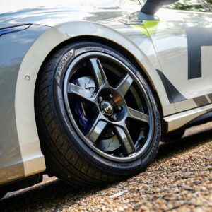 VWR610401_6jpg - OPSHOLDERS Close-up of a race car wheel with a Yokohama tire and alloy rim, parked on gravel, part of a white/gray race car body with large graphics.
