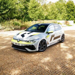 VWR610401_7jpg - OPSHOLDERS White hatchback with yellow and gray racing graphics parked on a gravel driveway with green trees in the background.