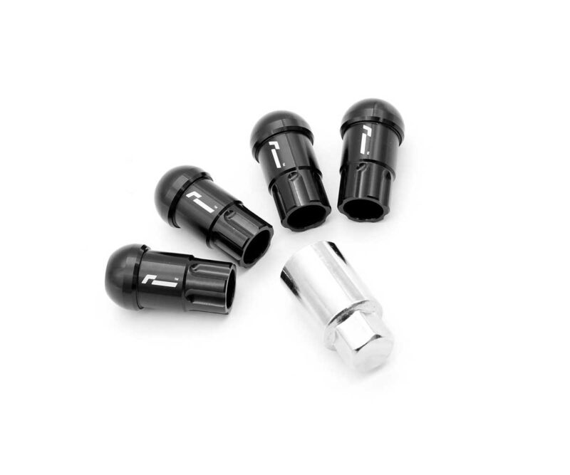 Five black bicycle valve cores with a silver adapter on a white background; arranged in a circular pattern, used to seal or adapt valve stems.