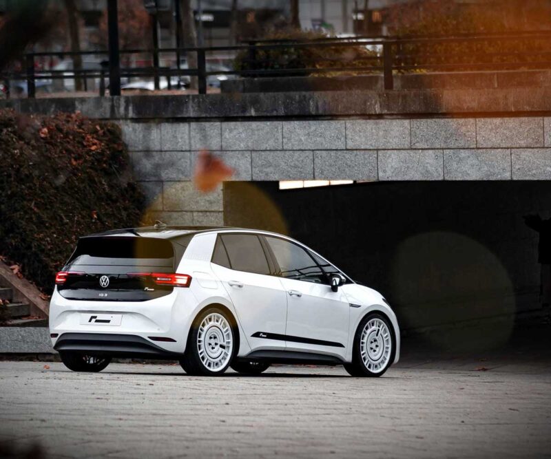 VW_ID3_Springs_1-1jpg - OPSHOLDERS White Volkswagen electric hatchback (ID.3) viewed from rear-three-quarters parked on a paved area near a tunnel in an urban setting, autumn leaves nearby.