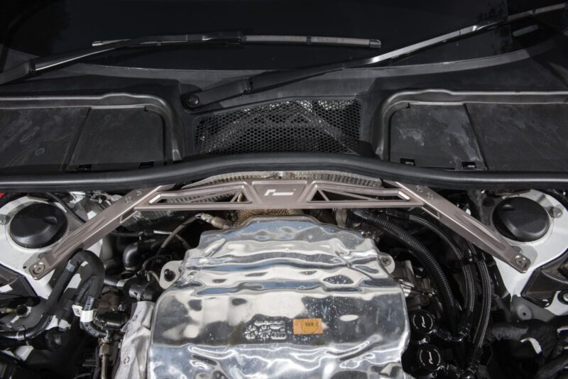 audi-b9-a4s4-strut-brace_42525934122_o-1jpg - OPSHOLDERS Under-hood view of a car engine bay with a silver crossmember brace spanning the front and various hoses visible beneath it