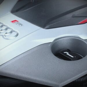 Close-up of an Audi R8 badge on the white hood with a circular fuel filler cap in the gray panel foreground.