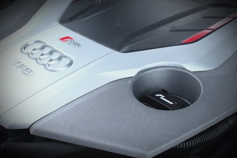Close-up of an Audi R8 badge on the white hood with a circular fuel filler cap in the gray panel foreground.