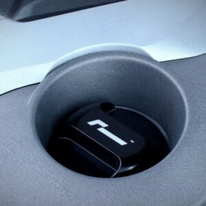 Close-up of a circular cup holder in a car’s center console, with a black insert bearing a white emblem.