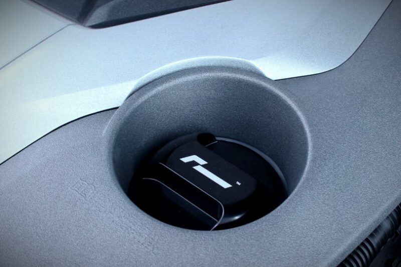 Close-up of a circular cup holder in a car’s center console, with a black insert bearing a white emblem.