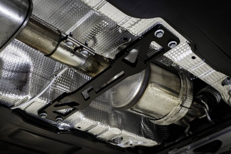 Underside of a car showing an exhaust pipe and mounting bracket with silver heat shielding above it